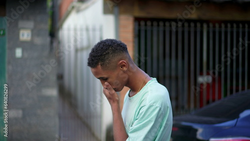 One pensive young black Brazilian man concerned about life while walking in urban street. Anxious African American descent person strolling in urban environment rubbing face and neck