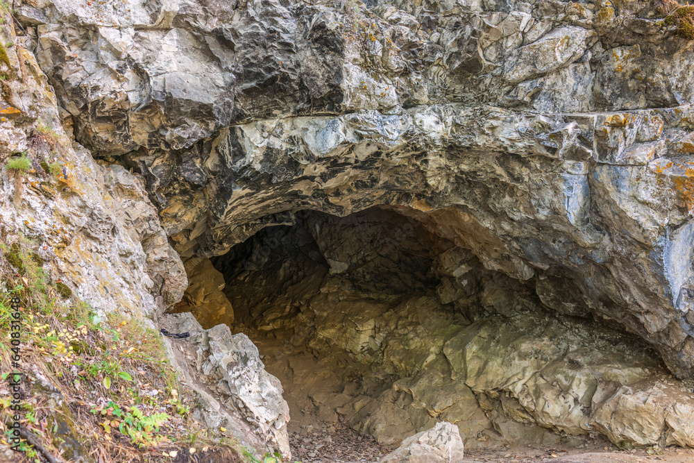 Limestone cliff wall with entrance of the cave. Cave in a layered limestone rock. Limestone cliff wall with entrance of the cave. Cave in a layered limestone rock.
