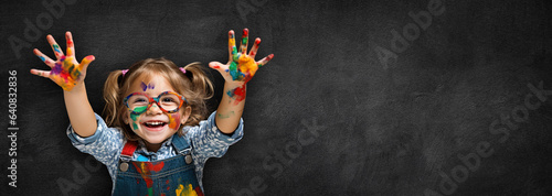 Smiling Little Girl in Glasses with Colorful Painted Hands on Black Textured Chalkboard
