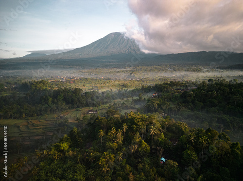 Aerial Vista of Bali s Largest Volcano Mount Agung  Shrouded in Morning Fog  Amidst Palms and Rice Fields. Sunrise in the Countryside. A Vacation Destination in Asia s Indonesia