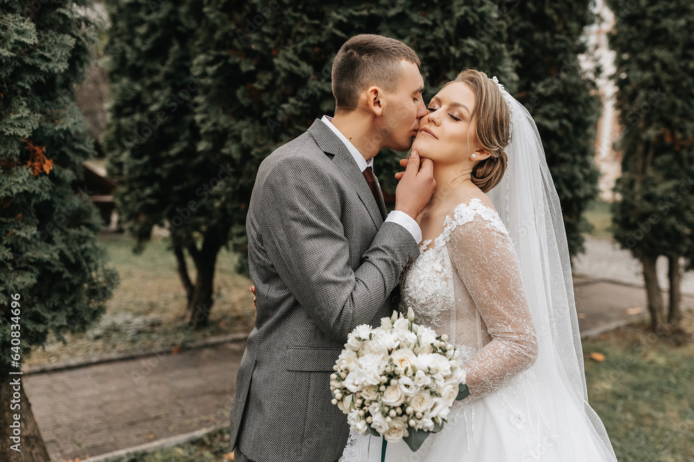 Stylish bride and groom tenderly embrace and kiss. Beautiful bride with modern bouquet embracing stylish groom in autumn park. Sensual romantic moment. Wedding. Stylish and beautiful. Stylish bride and groom tenderly embrace and kiss. Beautiful bride with modern bouquet embracing stylish groom in autumn park. Sensual romantic moment. Wedding. Stylish and beautiful.
