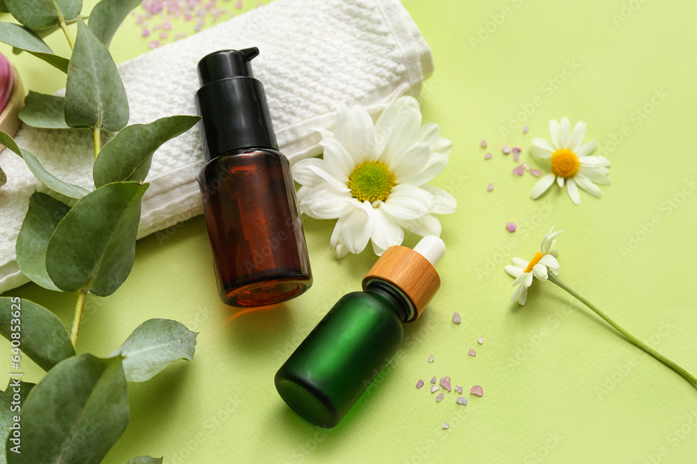 Composition with bottles of cosmetic products, clean towel and flowers on green background Composition with bottles of cosmetic products, clean towel and flowers on green background