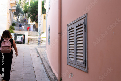 Fototapeta Naklejka Na Ścianę i Meble -  Closed wooden window in a soft orange wall in Athens, Greece while tourist walking in the streets