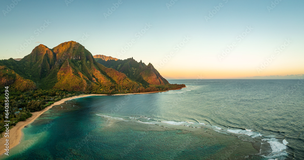 Aerial wide panoramic image of early morning light just catching the mountains dominating Tunnels beach on Kauai with Na Pali mountains