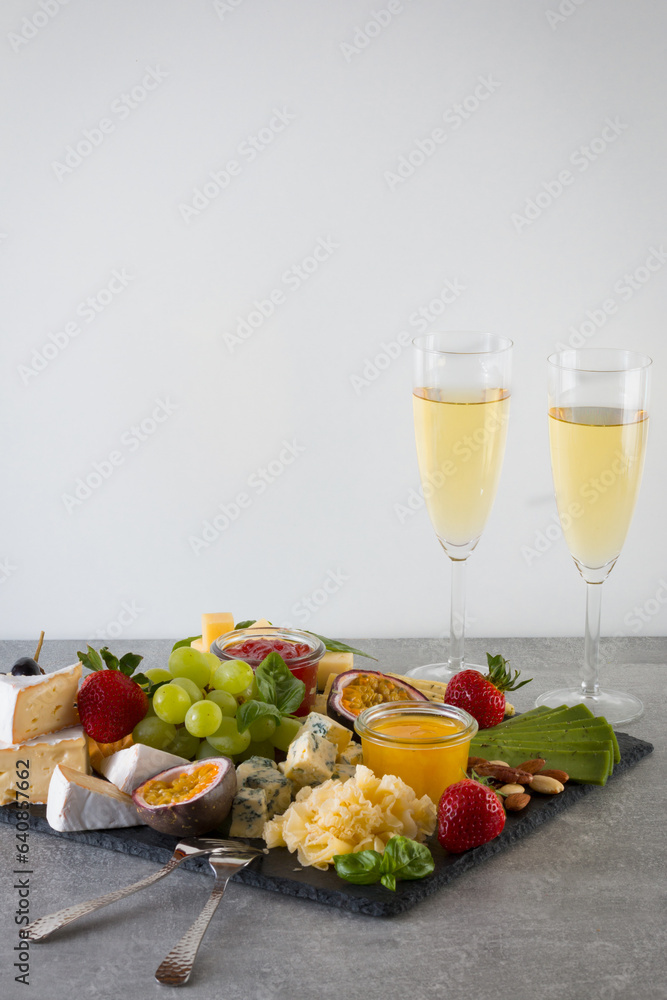 Platter with organic cheeses, fruits, berries and wine on a gray background. Delicious cheese appetizer.