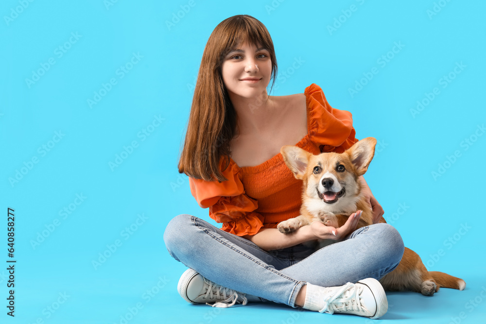 Pretty young woman sitting with cute Corgi dog on blue background Pretty young woman sitting with cute Corgi dog on blue background