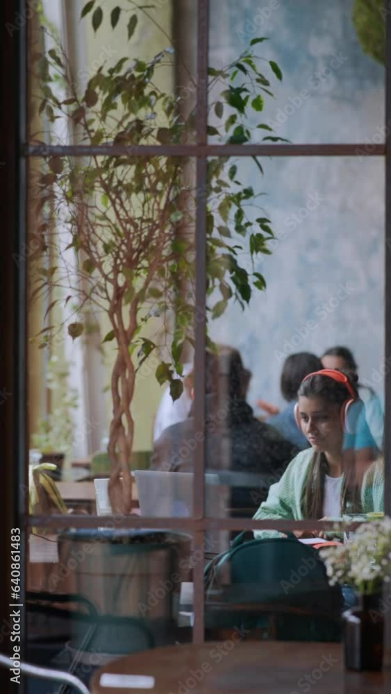A café backdrop presents a young and pretty girl using a laptop with headphones on. A café backdrop presents a young and pretty girl using a laptop with headphones on.