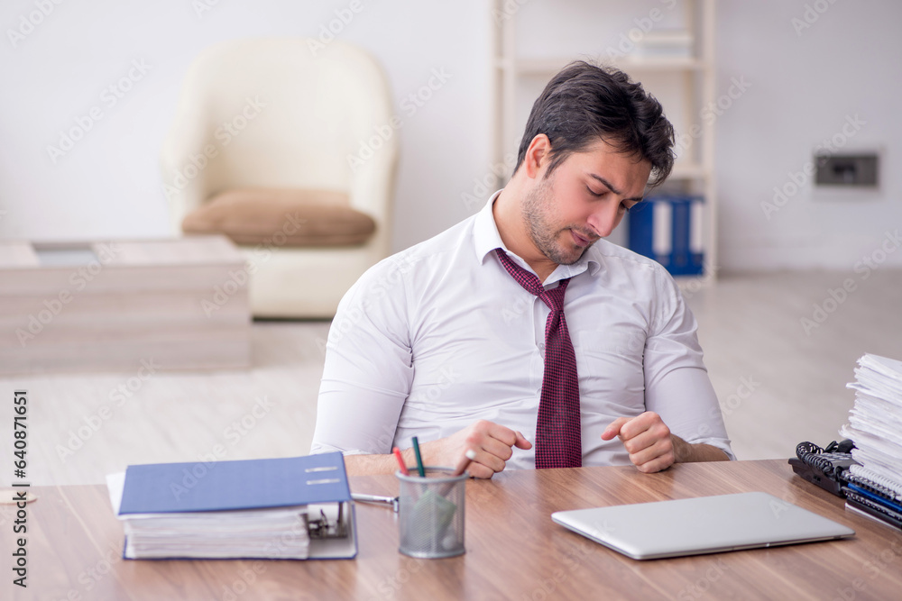 Young male employee unhappy with excessive work in the office Young male employee unhappy with excessive work in the office
