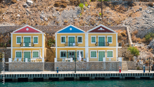 Three colorful houses located on a hill near the clear sea