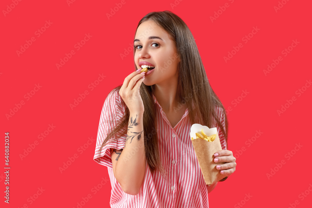 Beautiful young woman eating french fries on red background Beautiful young woman eating french fries on red background