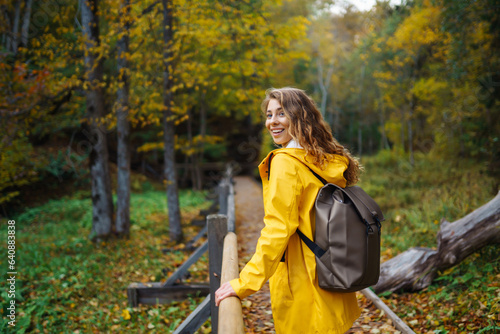 Autumn hike in nature. Woman in a yellow coat with a backpack walks along a wooden staircase  a path  enjoying the autumn scenery in the forest. Concept of nature  hiking  travel.