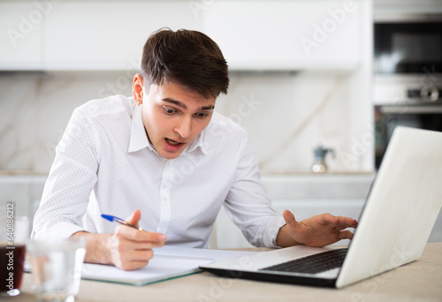 concentrated young man working on laptop and making notes in notebook