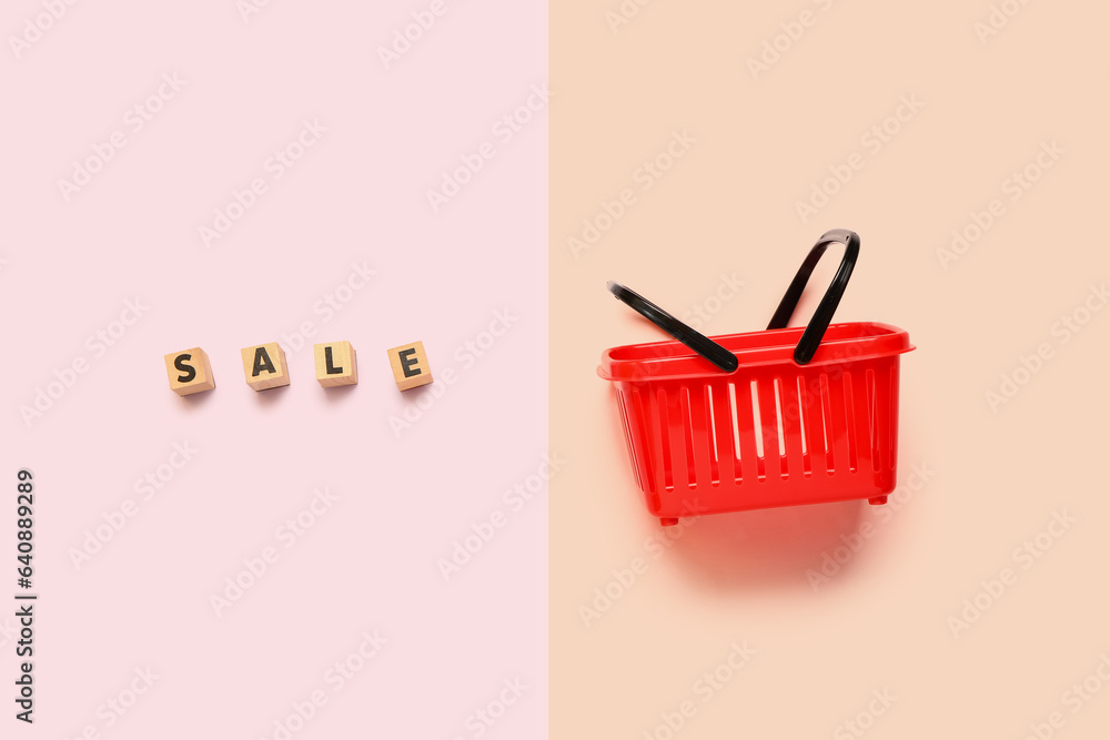 Fototapeta premium Small red shopping basket with text SALE on color background