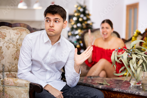 Disappointed young couple arguing among themselves before Christmas Eve while sitting on sofa in living room at home