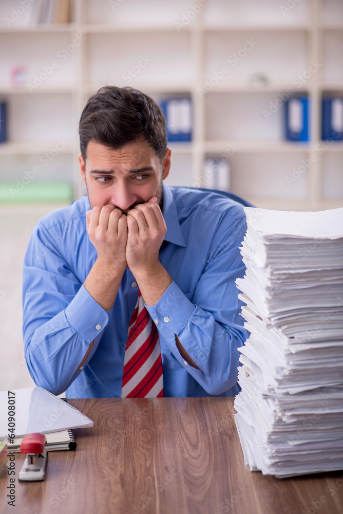 Young male employee unhappy with excessive work in the office Young male employee unhappy with excessive work in the office