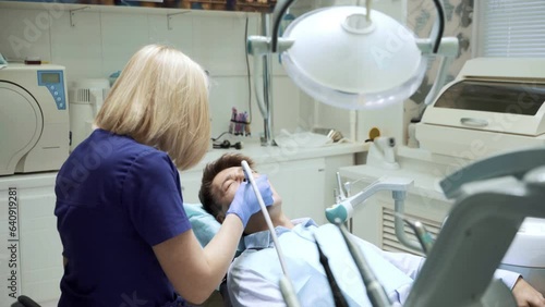 Portrait of young woman dentist sitting back examining teeth of male patient using mirror modern dentistry equipment in clinic hospital cabinet. Stomatoligy medical health care concept. Oral hygiene photo