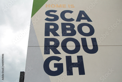 scarborough text caption writing written on side of building in four lines rows center frame in black capital letters on white background screen right with sky screen left photo