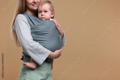 Mother holding her child in baby wrap on light brown background, closeup. Space for text