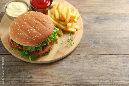Delicious burger with beef patty, sauce and french fries on wooden table, above view. Space for text