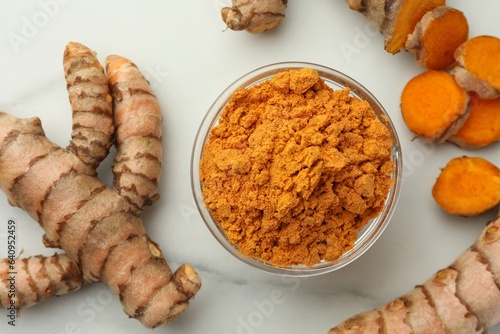Aromatic turmeric powder and raw roots on white marble table, flat lay