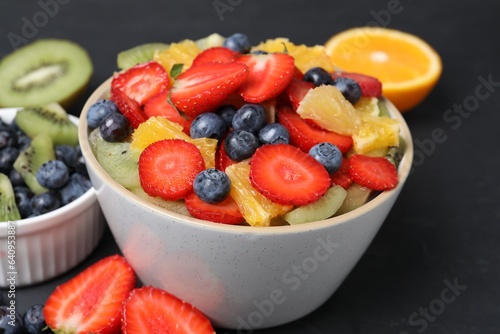Delicious fresh fruit salad in bowl and ingredients on dark table  closeup