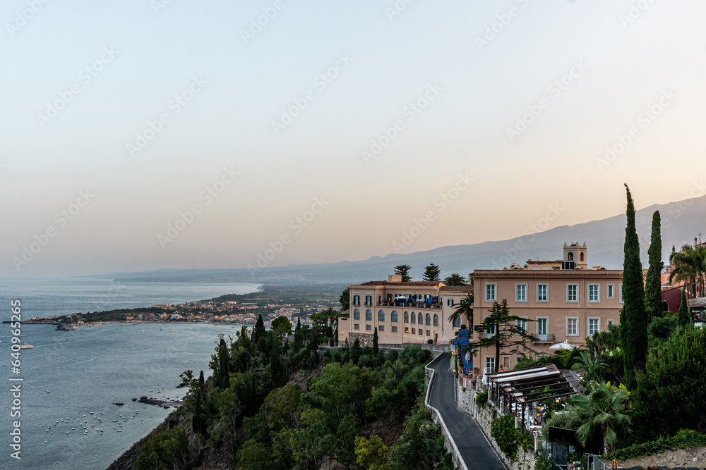 Hotel building in Taormina with accommodation for tourists near coast at sunset