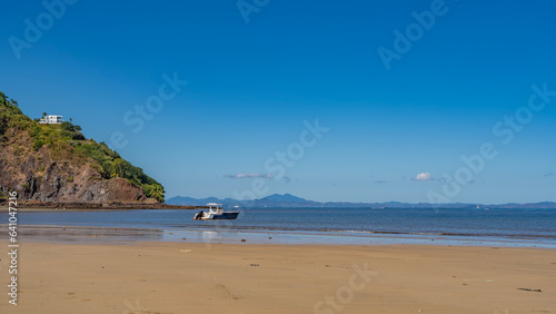 Sandy beach on a tropical island. The boat is moored in the blue ocean. The white building on the hill. A mountain range against the azure sky on the horizon. Madagascar. Nosy Be island.