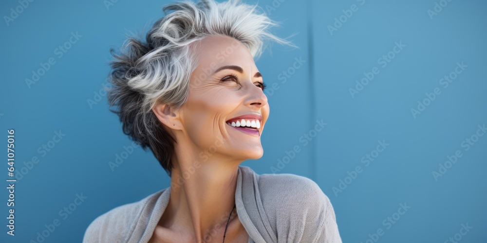 Psychology portrait of a happy smiling Scandinavian woman in her 50s. Luxurious middle-aged woman with a short gray hairdo looking at copy space. Photo on blue background.