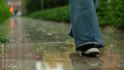 Female feet walking on the street on puddles. Woman steps by the wet road through the city under the rain. Rainy summer day, slow motion
