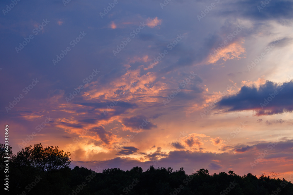 Colorful sunset and clouds in Wisconsin during summer with tree line silhouette
