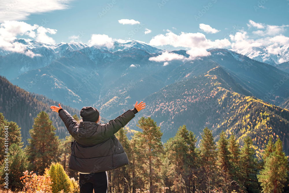 Naklejka premium Tourist woman enjoy view of the autumn mountains in Svaneti in Georgia. Snow-capped mountains and blue sky with clouds.