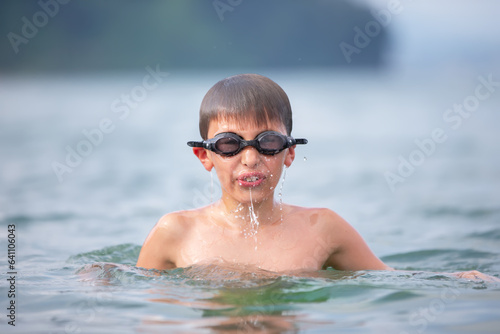 A boy in swimming goggles swims in the sea.