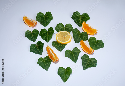 Fototapeta Naklejka Na Ścianę i Meble -  Leafs in the shape of a heart and a slice of fresh orange. Heartshaped isolated on a white background. Love Valentin's or Woman's Day concept. Flat lay. Natural green leaf.