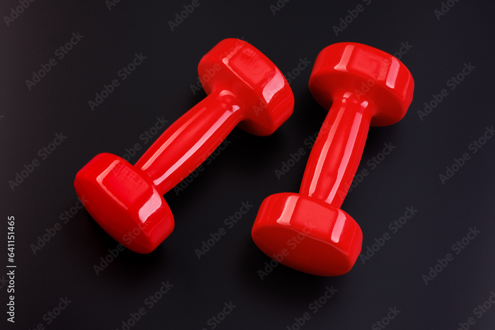 A pair of red dumbbells lies on a black matte surface. View from above. A pair of red dumbbells lies on a black matte surface. View from above.
