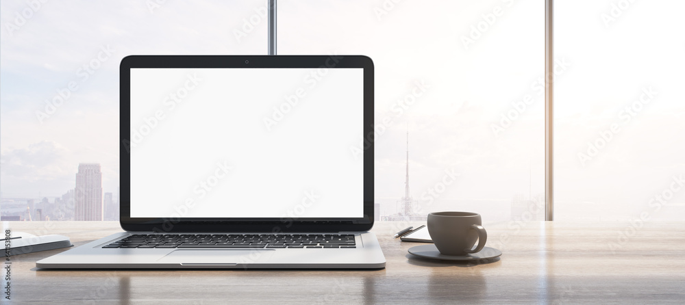 Fototapeta premium Wide image of laptop with empty white mock up monitor, coffee cup and notepad placed on wooden desktop. Window with bright city view in the background. 3D Rendering.