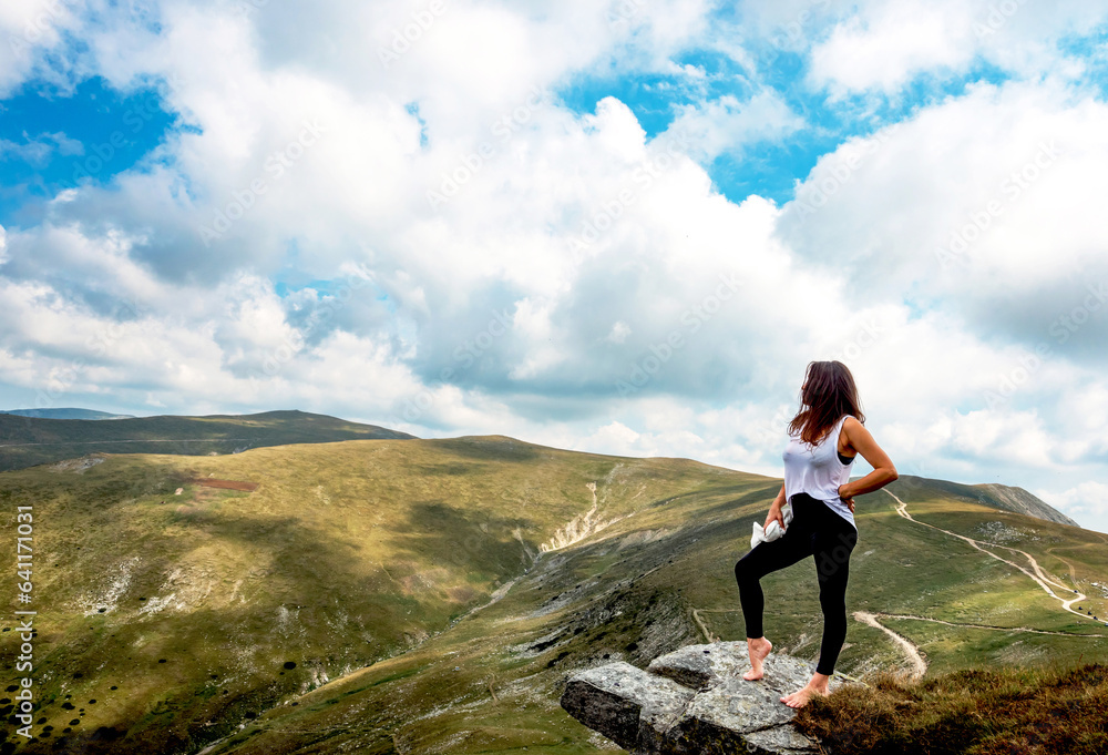 Obraz premium A young and beautiful woman sits on a rock and admires the mountain landscape. The young woman poses in a spectacular mountain setting.