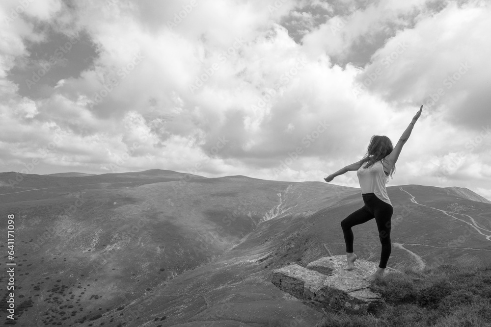 A beautiful woman is doing relaxation exercises, meditation on a rock, next to a precipice. The young woman poses in a spectacular mountain setting. A beautiful woman is doing relaxation exercises, meditation on a rock, next to a precipice. The young woman poses in a spectacular mountain setting.