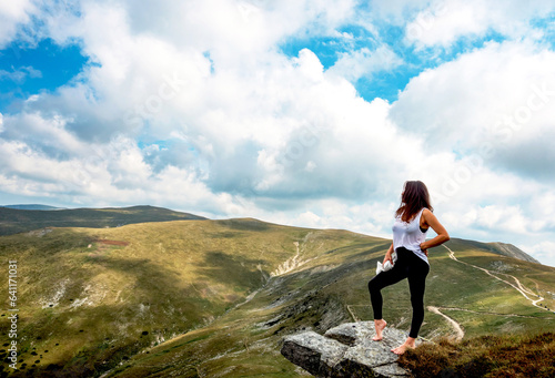 A young and beautiful woman sits on a rock and admires the mountain landscape. The young woman poses in a spectacular mountain setting.