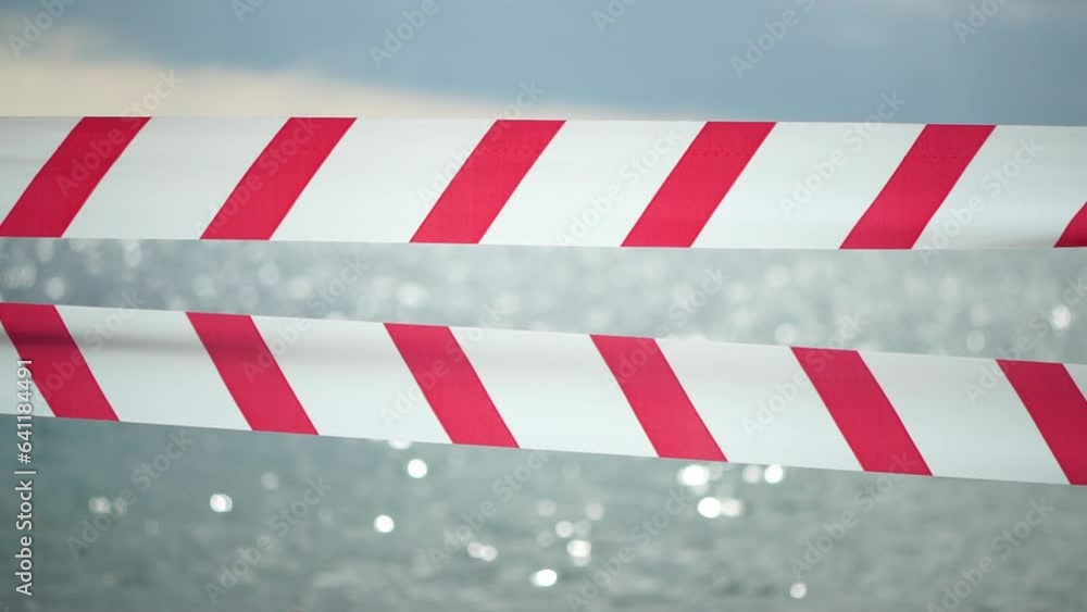 Red white warning tape barrier ribbon swinging in the wind across exotic sea beach background without people. No entry Red White caution tape. No holiday concept, delayed travel, no summer plans Red white warning tape barrier ribbon swinging in the wind across exotic sea beach background without people. No entry Red White caution tape. No holiday concept, delayed travel, no summer plans