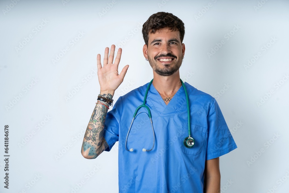 young caucasian doctor man wearing blue medical uniform showing and pointing up with fingers number five while smiling confident and happy. young caucasian doctor man wearing blue medical uniform showing and pointing up with fingers number five while smiling confident and happy.