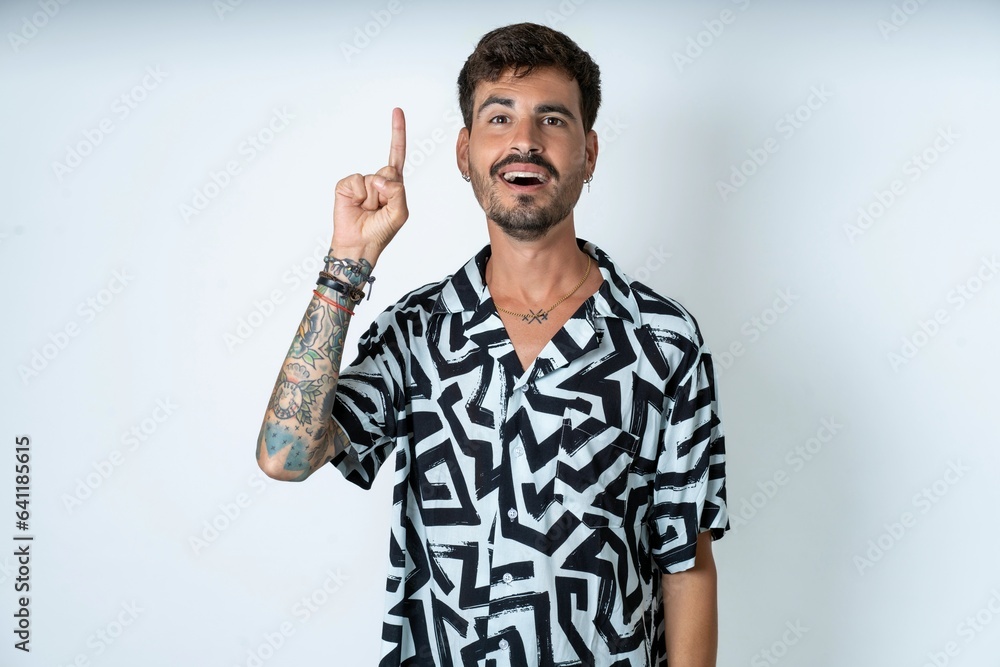 young caucasian man wearing printed shirt pointing finger up and looking inspired by genius thought, showing good idea sign, having clever solution in mind young caucasian man wearing printed shirt pointing finger up and looking inspired by genius thought, showing good idea sign, having clever solution in mind