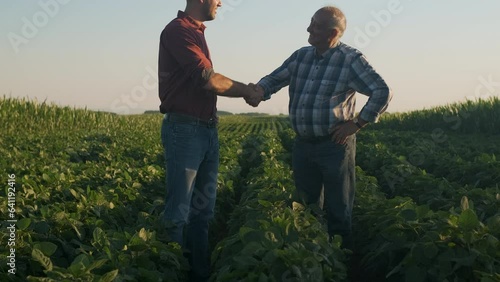 Two farmers standing in soy field making agreement with handshake at sunset.