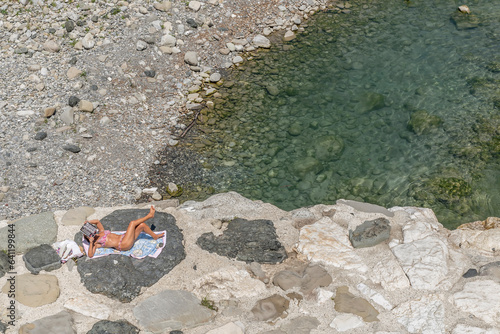 A woman sunbathes while reading a magazine lying on the rocks on the bank of the Trebbia river in Bobbio, Italy photo