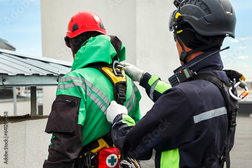 Men industry mountaineer climbers in work uniform, checks rope equipment partner for safety on roof house. Access workers high-rise dangerous job. Industrial urban works concept. Copy ad text space © Alex Vog