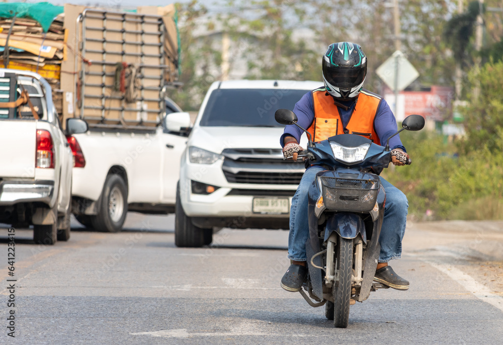 Fototapeta premium Front view of a man in an orange vest of a taxi driver riding a motorcycle, Bangkok, Thailand