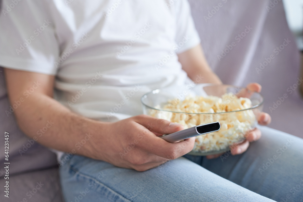 Obraz premium Man with remote control and bowl of popcorn at home, closeup