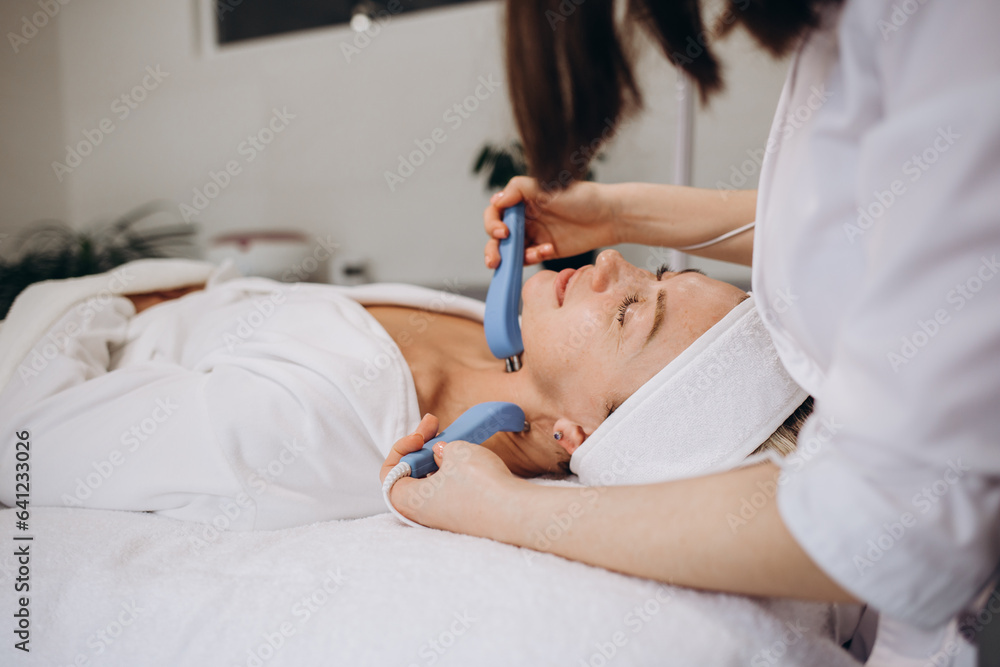 Obraz premium Woman getting microcurrent procedure facelift. Beautician doing anti-aging, to perform facial tightening and toning.