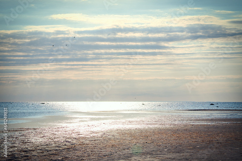 Sunset, illuminated sea. Sandy beach in the foreground. Light waves. Baltic Sea