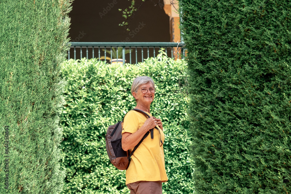 Happy senior tourist woman in yellow enjoying the journey visiting gardens of Alcazar, a historic famous place residence in Seville, Spain - travel vacation concept