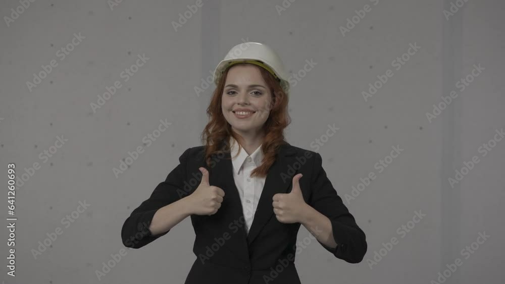 The female architect points to herself and gives a thumbs up, and crosses her arms over her chest. I am the best. Business woman in a protective white hard hat in the studio on a gray background. HDR The female architect points to herself and gives a thumbs up, and crosses her arms over her chest. I am the best. Business woman in a protective white hard hat in the studio on a gray background. HDR